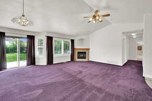 Unfurnished living room with vaulted ceiling, carpet, ceiling fan, baseboards, and a warm lit fireplace