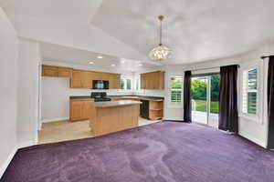 Kitchen with black appliances, a center island, vaulted ceiling, light carpet, and healthy amount of natural light