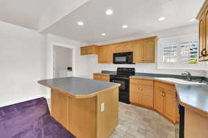 Kitchen featuring black appliances, a sink, washer and clothes dryer, recessed lighting, and a kitchen island