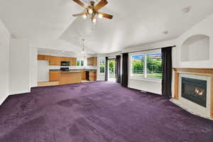 Unfurnished living room with carpet, a tile fireplace, lofted ceiling, ceiling fan, and baseboards
