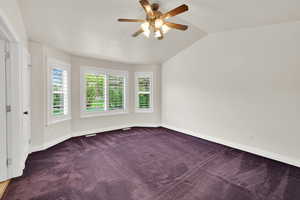Carpeted spare room featuring ceiling fan, baseboards, and vaulted ceiling