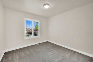 Unfurnished room featuring dark colored carpet and baseboards