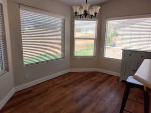 Unfurnished dining area featuring dark wood-type flooring, a chandelier, and baseboards