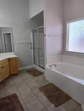 Bathroom featuring tile patterned floors, vanity, a stall shower, a bath, and baseboards
