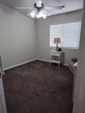 Unfurnished room featuring a ceiling fan, dark carpet, and baseboards