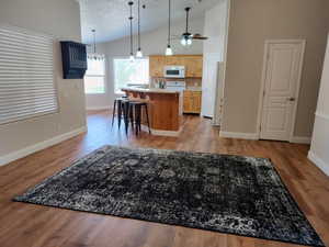Kitchen with white microwave, light brown cabinetry, vaulted ceiling, an island with sink, and baseboards