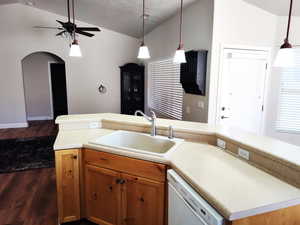 Kitchen with dishwasher, a sink, vaulted ceiling, dark wood finished floors, and ceiling fan