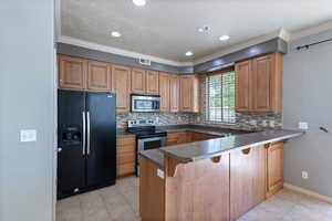 Kitchen featuring stainless steel appliances, a peninsula, a kitchen bar, backsplash, and ornamental molding