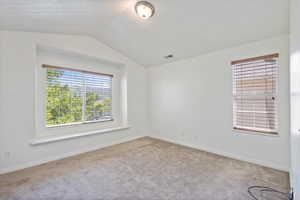 Carpeted empty room featuring lofted ceiling and baseboards