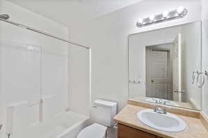 Full bathroom with toilet, a textured ceiling, vanity, and shower / washtub combination