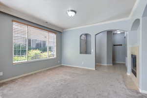 Unfurnished living room with carpet flooring, crown molding, a textured ceiling, arched walkways, and a tiled fireplace