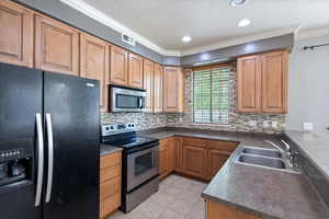 Kitchen featuring stainless steel appliances, a sink, dark countertops, crown molding, and decorative backsplash