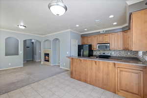 Kitchen with appliances with stainless steel finishes, light colored carpet, baseboards, a peninsula, and light tile patterned floors