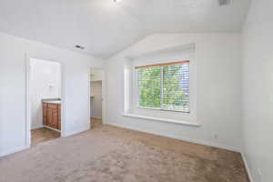 Unfurnished bedroom with light carpet, a spacious closet, lofted ceiling, baseboards, and ensuite bathroom