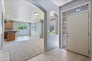 Entryway with light colored carpet, light tile patterned flooring, baseboards, arched walkways, and a textured ceiling