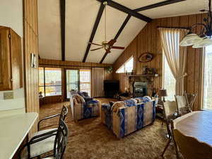 Living area with wood walls, dark carpet, a ceiling fan, a fireplace, and high vaulted ceiling