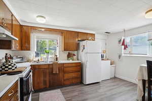 Kitchen with white appliances, light countertops, brown cabinetry, light wood-style flooring, and under cabinet range hood