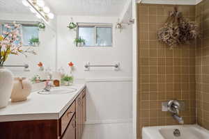 Full bathroom with vanity, wainscoting, bathtub / shower combination, a textured ceiling, and baseboards