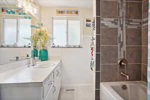Bathroom featuring vanity, healthy amount of natural light, wainscoting, shower / bathtub combination, and tile patterned flooring