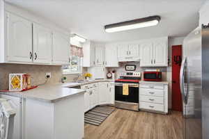 Kitchen featuring appliances with stainless steel finishes, under cabinet range hood, a sink, a peninsula, and white cabinetry