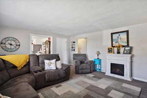Living room featuring a textured ceiling, carpet flooring, a warm lit fireplace, and baseboards