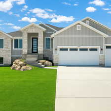 View of front of house with stone siding, board and batten siding, an attached garage, driveway, and a front yard