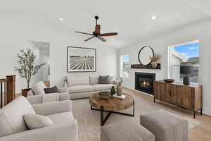 Living room with ceiling fan, light wood-type flooring, lofted ceiling, a glass covered fireplace, and recessed lighting