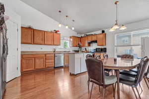 Kitchen with appliances with stainless steel finishes, light wood-style flooring, brown cabinets, hanging light fixtures, and high vaulted ceiling