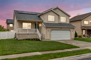 Split level home featuring covered porch, stucco siding, roof mounted solar panels, an attached garage, and a shingled roof