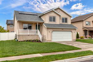 Tri-level home with covered porch, stucco siding, roof mounted solar panels, a shingled roof, and a garage