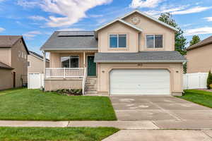 Tri-level home with covered porch, stucco siding, roof mounted solar panels, and roof with shingles