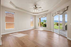 Unfurnished room with a tray ceiling, a ceiling fan, baseboards, and hardwood / wood-style floors