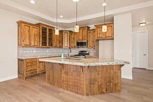 Kitchen with appliances with stainless steel finishes, brown cabinetry, light wood-type flooring, baseboards, and tasteful backsplash