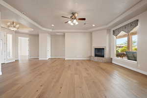 Unfurnished living room featuring a raised ceiling, light wood-style flooring, ceiling fan, a tile fireplace, and recessed lighting