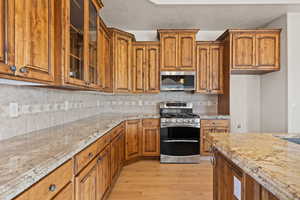 Kitchen with appliances with stainless steel finishes, light wood finished floors, light stone countertops, and brown cabinetry