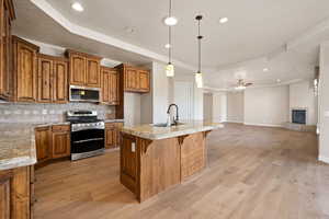 Kitchen with stainless steel appliances, a tray ceiling, brown cabinetry, a sink, and tasteful backsplash