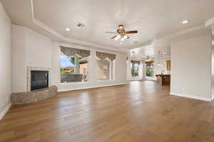 Unfurnished living room with a ceiling fan, a tray ceiling, hardwood / wood-style flooring, baseboards, and recessed lighting