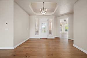 Foyer entrance featuring a raised ceiling, a chandelier, baseboards, and hardwood / wood-style flooring