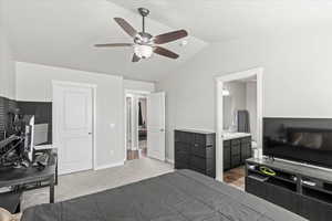 Carpeted bedroom featuring a sink, ceiling fan, vaulted ceiling, and ensuite bath
