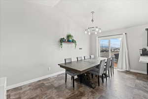 Dining space with stone finish floor, visible vents, vaulted ceiling, baseboards, and a notable chandelier