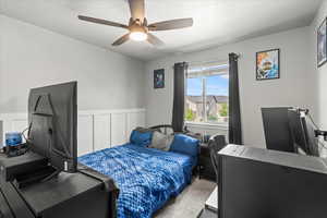Carpeted bedroom featuring ceiling fan and a wainscoted wall