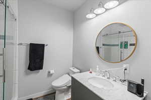Bathroom featuring vanity, baseboards, a stall shower, and toilet