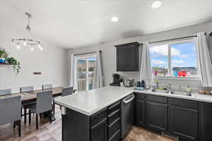 Kitchen with dishwasher, a sink, light countertops, a peninsula, and dark cabinetry