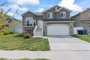 Split level home with a garage, a front lawn, stucco siding, and driveway