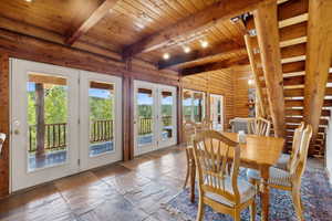 Dining space with french doors, wooden ceiling, rustic walls, beamed ceiling, and healthy amount of natural light