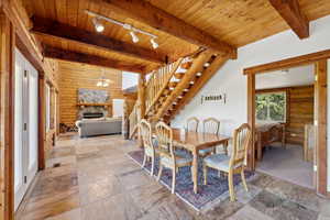 Dining room with rail lighting, beam ceiling, log walls, stairs, and a stone fireplace