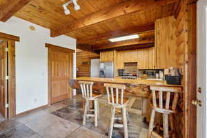 Kitchen featuring stainless steel appliances, beamed ceiling, wooden ceiling, a peninsula, and baseboards
