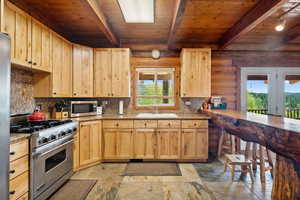 Kitchen featuring appliances with stainless steel finishes, light brown cabinets, rustic walls, wood ceiling, and a sink