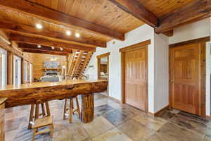 Recreation room with baseboards, beamed ceiling, wood ceiling, stone finish floors, and a fireplace