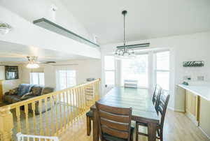 Dining space featuring light wood-type flooring, a chandelier, ceiling fan, and high vaulted ceiling